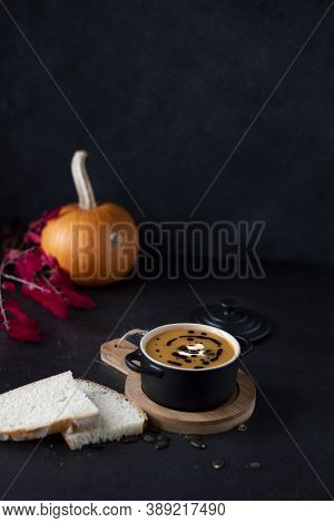 A Bowl With Orange Pumpkin Soup On Wood With Orange Pumpkin And Red Leabes On Black Background, Copy