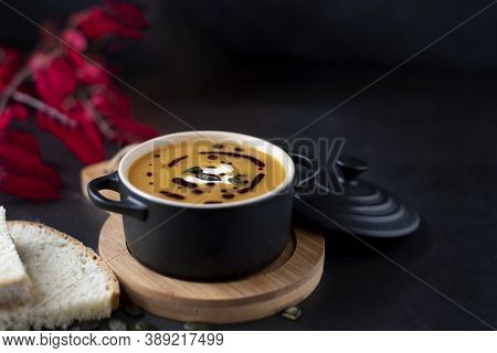 A Bowl With Orange Pumpkin Soup On Wood With Orange Pumpkin And Red Leabes On Black Background, Copy