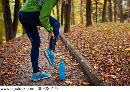 Runner Injured Leg During Workout Exercises In Autumn Park. Woman Feels Ankle Pain And Crick.