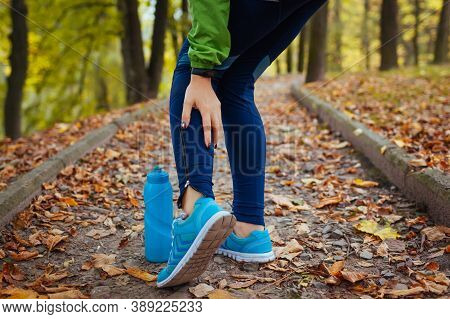 Young Runner Injured Leg During Workout Exercises In Autumn Park. Woman Feels Ankle Pain And Crick. 