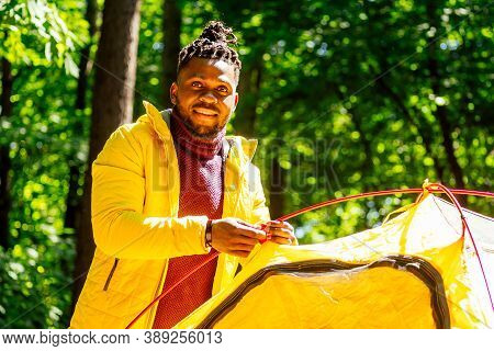 African American In Yellow Jacker Putting On A Tent In Forest
