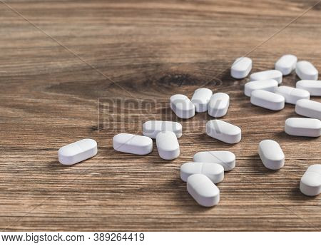 Medical Background. Several White Capsule Tablets Or Pills Scattered On Wooden Table. Healthcare Pha