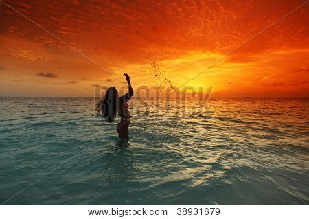 Vrolijke vrij jonge vrouw splashin in zee op zonsondergang
