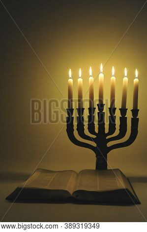 Menorah And Open Bible With 7 Lighted Candles Isolated On Golden Background. Vertical Shot.