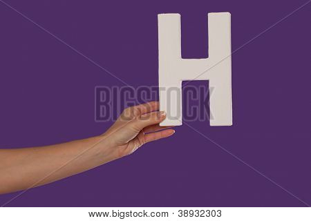 Vrouwelijke hand houden van de hoofdletters capital letter H geïsoleerd tegen een paarse achtergrond conceptua