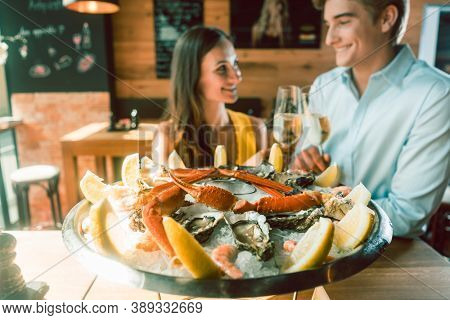 Close-up of fresh oysters and crabs served on ice with slices of lemon at the table of a romantic young couple eating at restaurant