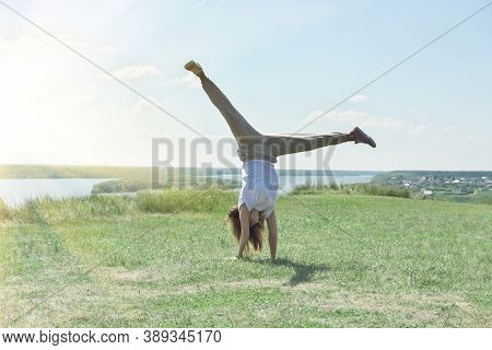 Toned Fit Woman Of Mid Age Turning Handsprings Or Cartwheel On A River Bank. Sunny Weather And Pleas