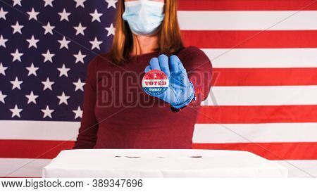 Woman Voting With Gloves And Face Mask And Showing I Voted Today Button With American Flag.