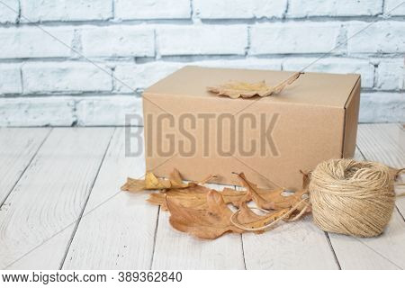 Cardboard Box, Autumn Oak Leaves And A Ball Of Rope On The Background Of A Wooden Table Top And A Li