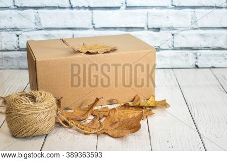 Cardboard Box, Autumn Oak Leaves And A Ball Of Rope On The Background Of A Wooden Table Top And A Li