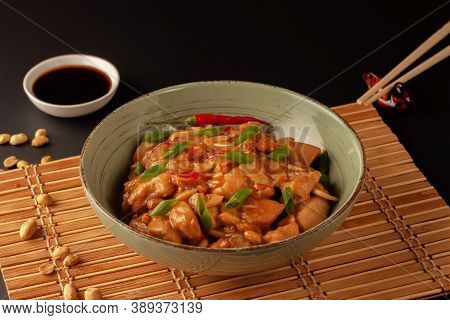 Kung Bao Chicken On A Black Background. A Chinese Dish With Chicken, Chili, Peanuts, Sauces And Onio
