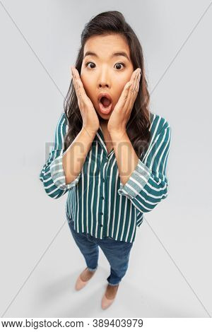 emotion, expression and people concept - impressed or shocked asian woman with open mouth goggling over grey background