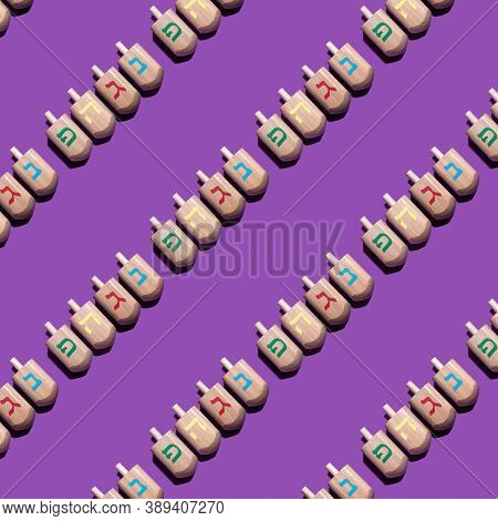Seamless Pattern With Hanukkah Dreidels On Violet Background. Hebrew Letters On Dreidels Say: 