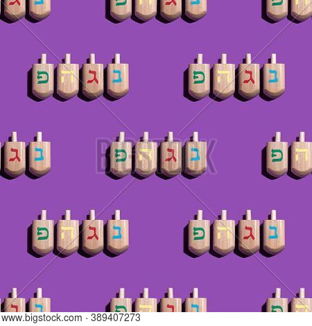 Seamless Pattern With Hanukkah Dreidels On Violet Background. Hebrew Letters On Dreidels Say: 