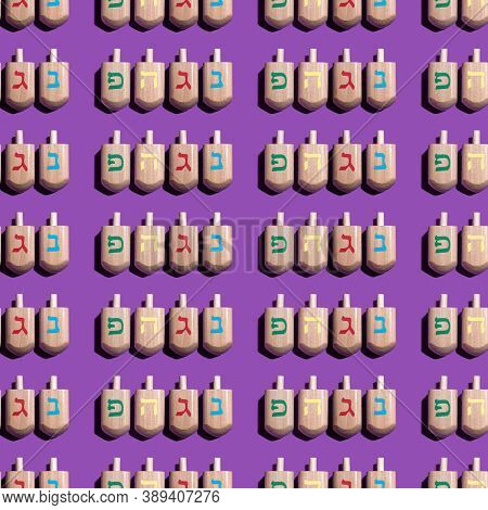 Seamless Pattern With Hanukkah Dreidels On Violet Background. Hebrew Letters On Dreidels Say: 