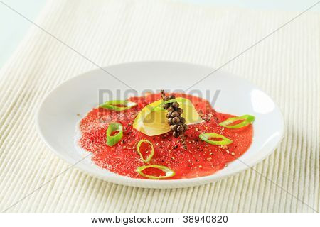 skivad carpaccio med citron och hela peppar, på den vita plattan