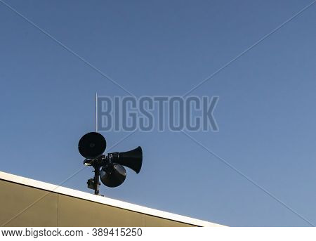Three Black Modern Megaphones Loudspeaker On The Building Roof Over Bluue Sky