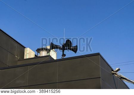 Three Black Modern Megaphones Loudspeaker On The Building Roof Over Bluue Sky