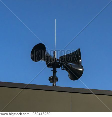 Three Black Modern Megaphones Loudspeaker On The Building Roof Over Bluue Sky