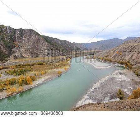 A Swift, Turbulent Turquoise River Flows Through An Autumn Valley Surrounded By Mountain Peaks.