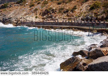 Sea Water Beats Against Rocky Rocks And Makes Waves With Foam, Rugged Pier In The Sea