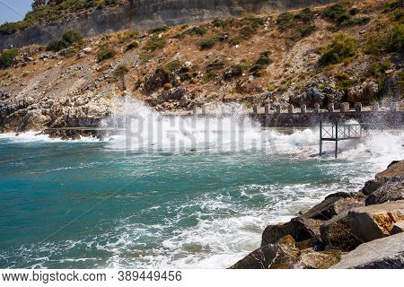 Sea Water Beats Against Rocky Rocks And Makes Waves With Foam, Rugged Pier In The Sea