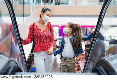 Mother And Daughter With Face Mask On Escalator Indoors In Shopping Center, Coronavirus Concept.