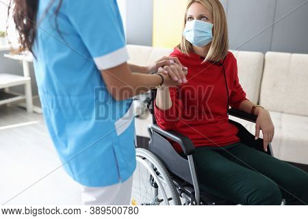 Doctor In Uniform Holds Hand Of Sick Young Woman In Wheelchair Portrait. Psychological Assistance To