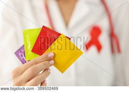 Infectious Disease Doctor With Red Ribbon On Uniform Holds Lot Of Condoms In Hand Closeup. Preventio