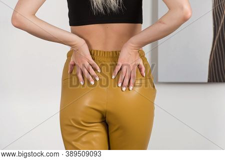 Stylish Beautiful Young Blond Woman In A Tight Yellow Pants, Black Top And White Shirt Near A White 