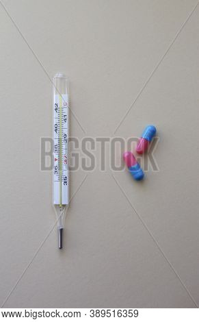 Thermometer And Pills On Neutral Background. First Aid, Care During Illness.