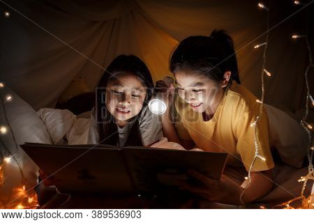 Family Concept. Elder Sister And Sister Reading Book With Flashlight Together Before Bedtime. Sister