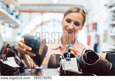 Woman shoemaker taking shoes to be repaired off the shelf in her workshop