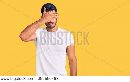 Young latin man wearing casual clothes covering eyes with hand, looking serious and sad. sightless, hiding and rejection concept 