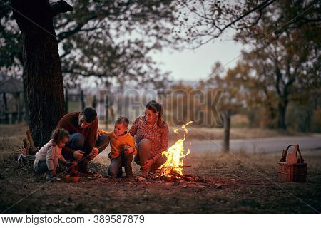 A happy family enjoying together around campfire in the forest on a beautiful autumn dusk