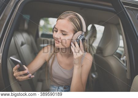 Cute teenage girl listening to her favorite music/audiobook on hig-end headphones during a roadtrip