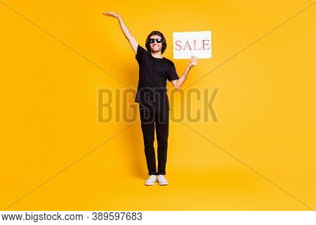 Full Legth Photo Of Young Man Stand Hold Poster Sale Raise Hand Empty Space Wear Black T-shirt Pants