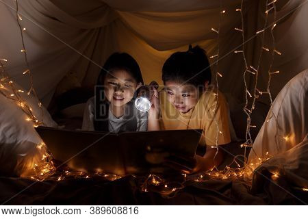 Family Concept. Elder Sister And Sister Reading Book With Flashlight Together Before Bedtime. Sister