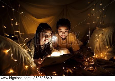 Family Concept. Elder Sister And Sister Reading Book With Flashlight Together Before Bedtime. Sister