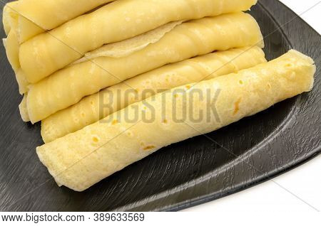 Closeup Of A Pile Of Rolled Maida Dosa Filled With Sweetened Grated Coconut On A Black Plate