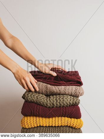 A Woman Takes A Sweater From A Stack Of Warm Things On A White Background. Faceless. Autumn Color Pa