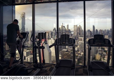 A Man On Fitness Equipment In Fitness Club With Bangkok City View Background From The Vindows
