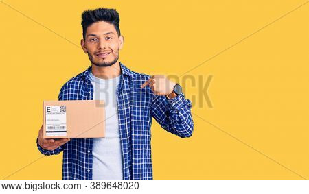 Handsome latin american young man holding delivery package pointing finger to one self smiling happy and proud 