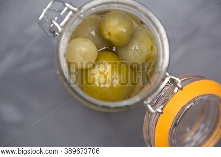 Pickled Green Small Tomatoes In A Glass Jar With A Lid On A Gray Background. Salted Cherries, Home-m