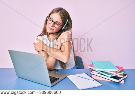Young blonde girl wearing operator headset at the call center office hugging oneself happy and positive, smiling confident. self love and self care 