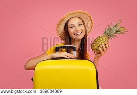 Pretty Young Woman With Pineaaple And Yellow Luggage Posing Over Pink Studio Background, Copy Space.