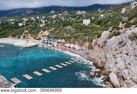 Suspension Bridge To The Diva Rock, Black Sea Coast, Near Yalta, Crimea. Panorama Of The Town Of Sim