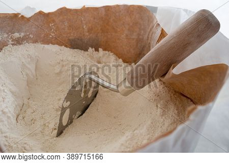 Close-up Of Plaster Trowel In Full Open Paper Bag Of Putty Powder For Wall Decoration,caulk Or Glaze