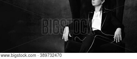 Black And White Cropped Photo Of A Woman In A Black Pantsuit Sitting In A High Chair In A Comfortabl
