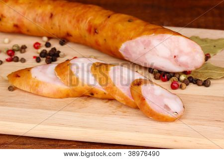 Tasty sausage on chopping board on browm background